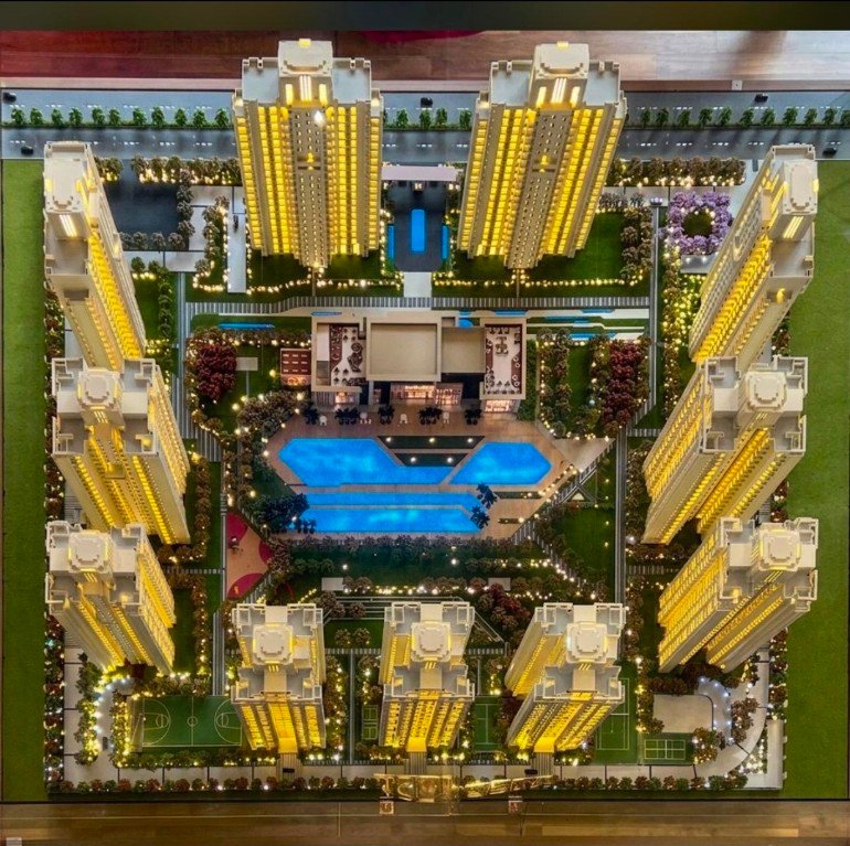 Aerial view of a high-rise residential complex with illuminated towers surrounding a central blue pool and green courtyards around it.